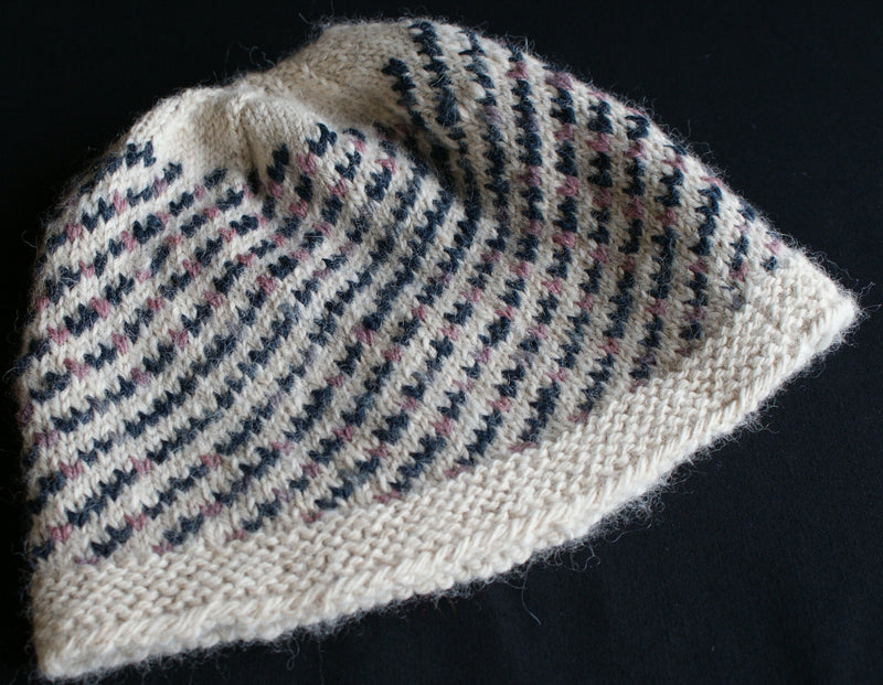 A cream coloured hat with diagonal stripes of blue and pink stitches