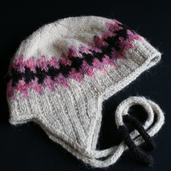A cream coloured hat with pink and black decorative bands knit in. The ties have black tips on the end